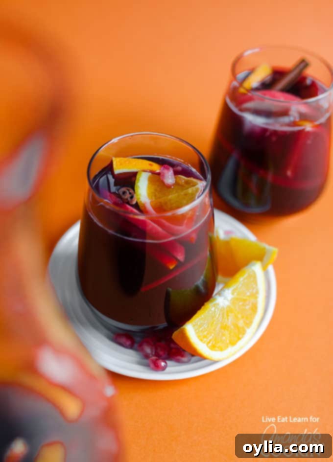 Glass of vibrant Pomegranate Sangria garnished with a fresh orange slice, perfect for holiday celebrations.