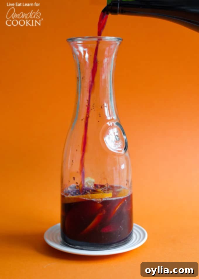 Pouring homemade Pomegranate Sangria into a large pitcher with fresh fruit.