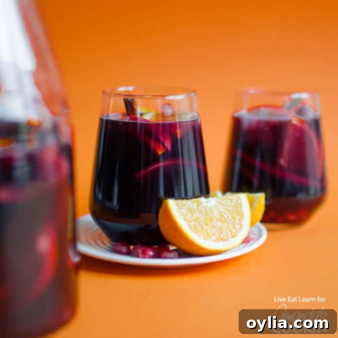 Close-up of a glass of Pomegranate Sangria with an orange wedge garnish.