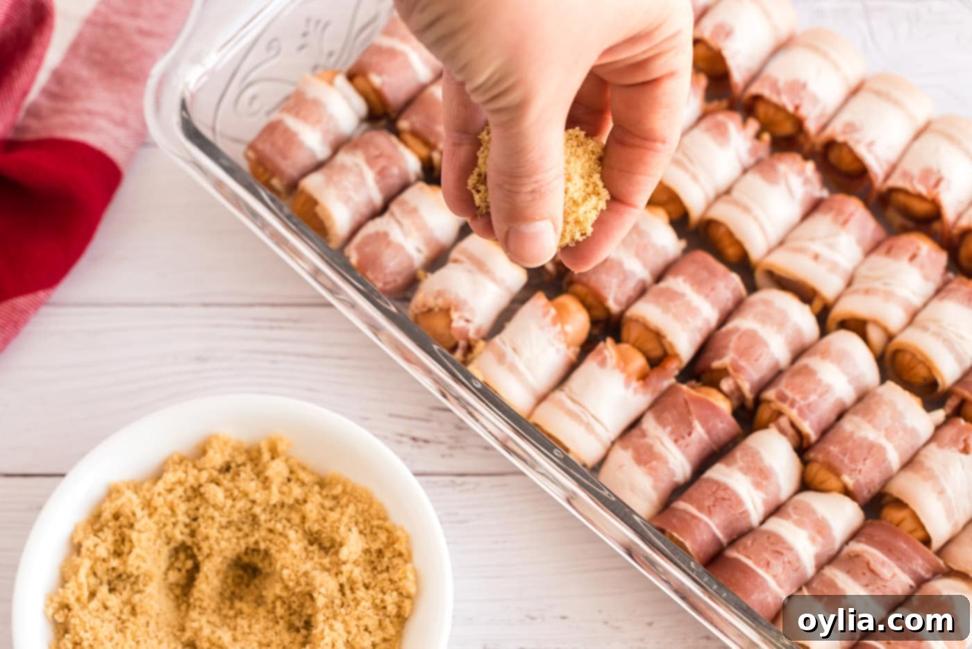 Brown sugar being sprinkled generously over Bacon Wrapped Little Smokies in a baking dish