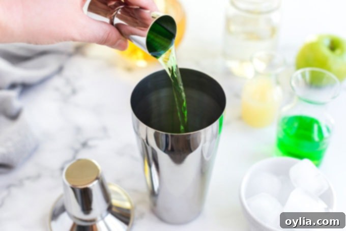 pouring apple vodka into a cocktail shaker