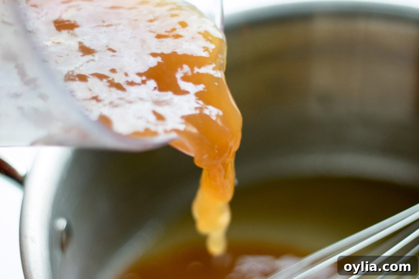 Adding rich pan drippings to the roux in a saucepan, whisking continuously