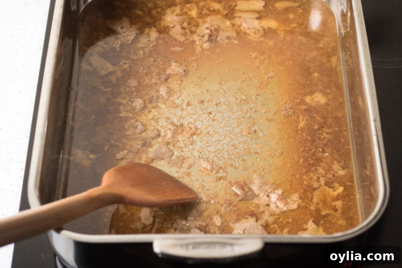 Spatula scraping delicious pan drippings from the bottom of a roasting pan