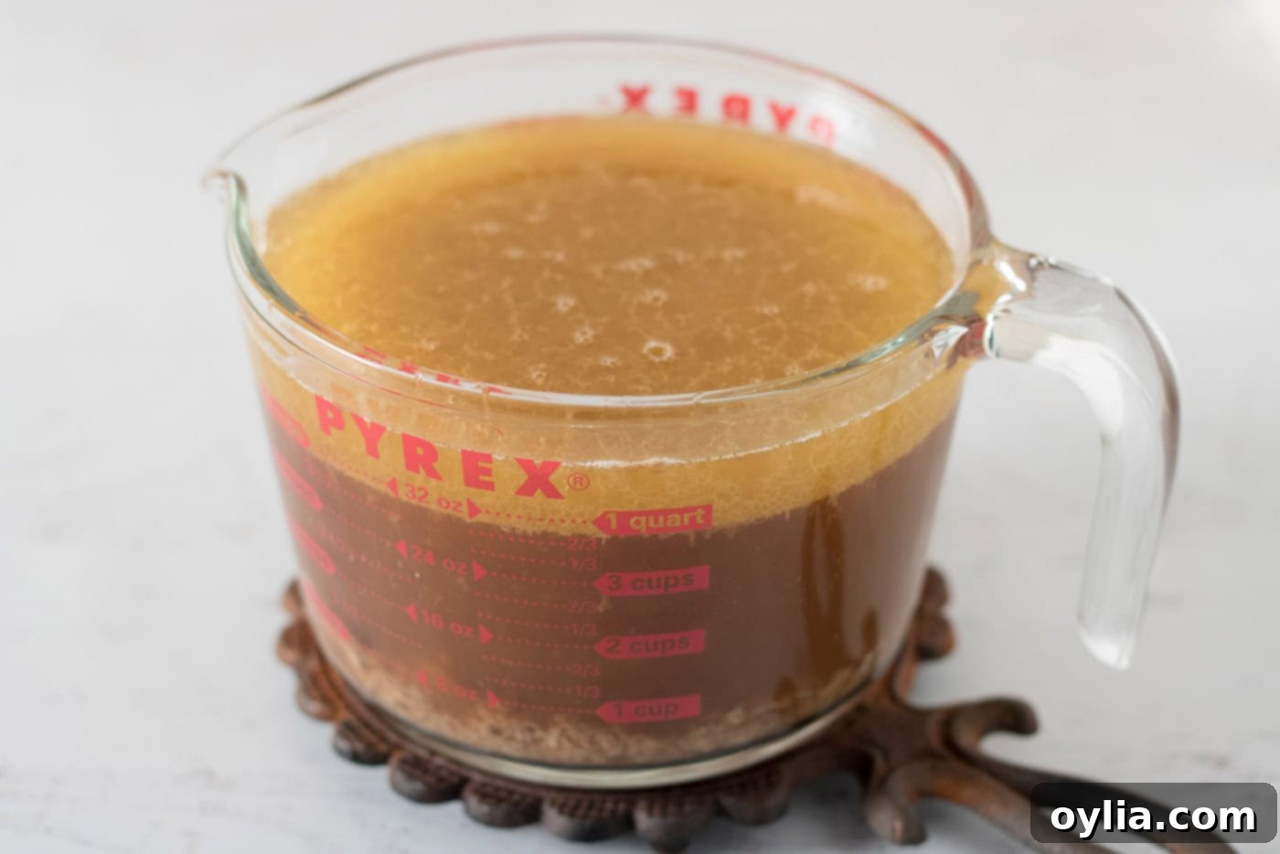 Wet measuring cup containing broth and rich roasted turkey drippings, cooling to separate fat