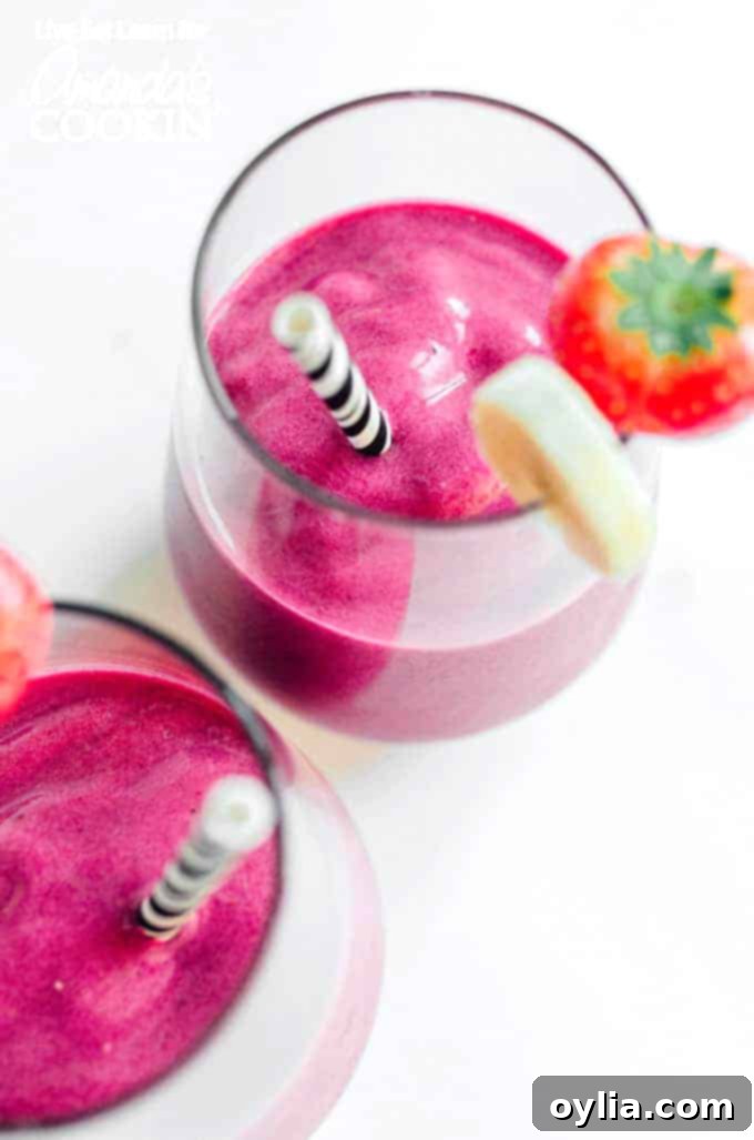 A tall glass of vibrant pink Strawberry Beet Smoothie with a straw, garnished with fresh strawberries and a beet slice, against a light background.