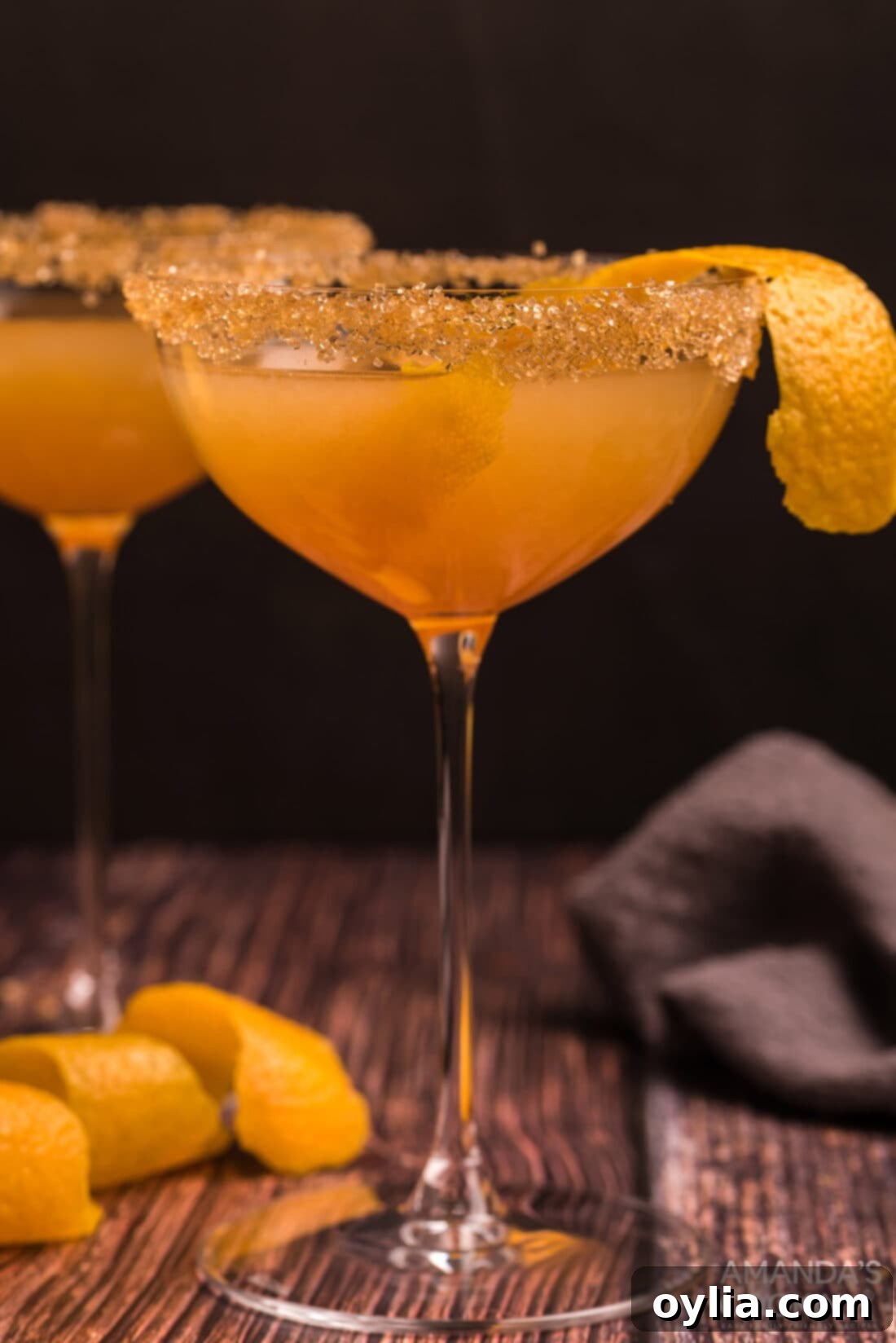 Close up photo of a Sidecar Cocktail, showcasing its amber hue and orange peel garnish in a coupe glass.