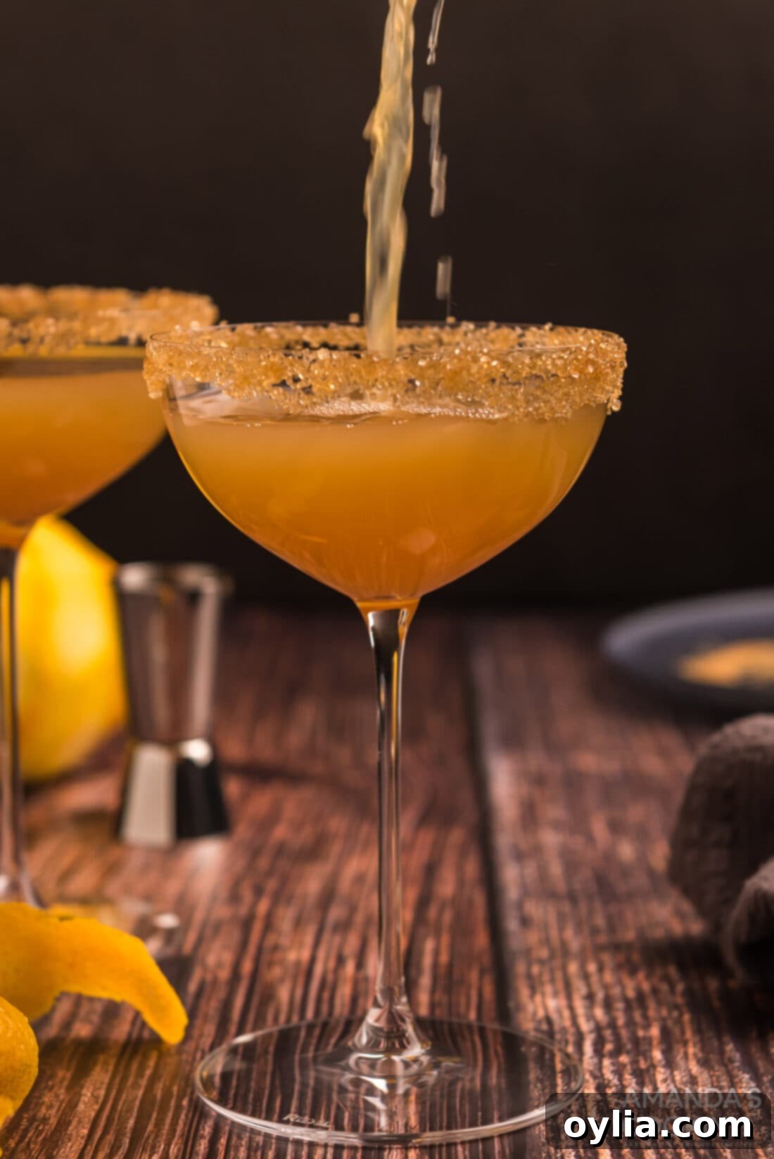 A bartender pouring a Sidecar cocktail from a shaker into a chilled coupe glass.