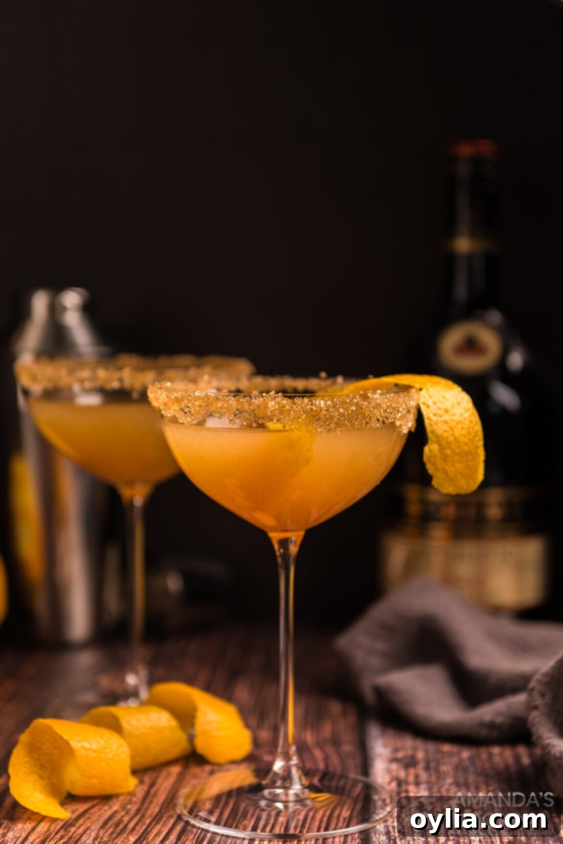 A vibrant citrus cocktail in a coupe glass with an orange peel garnish, set against a blurred background.