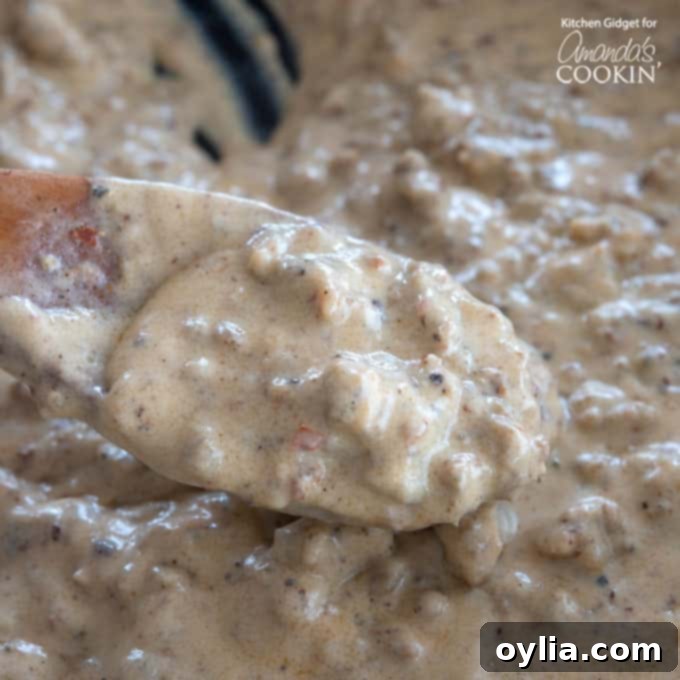 Close-up of golden brown sausage gravy simmering in a cast iron skillet with a wooden spoon