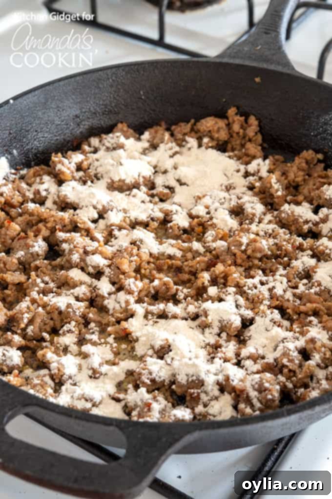 Flour being stirred into browned sausage and butter in a skillet to form a roux for the gravy