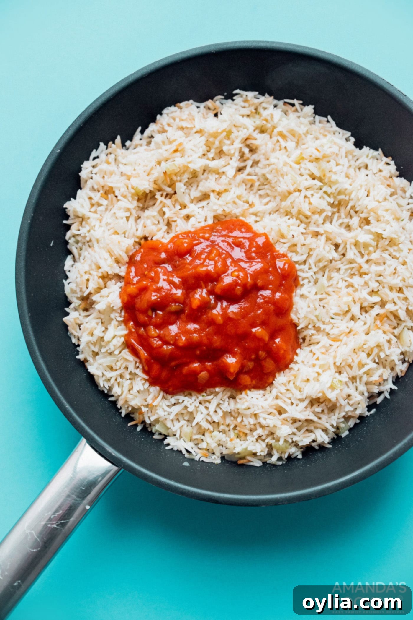 Close-up of rice grains mixed with diced tomatoes and spices, showing the rich color before cooking.