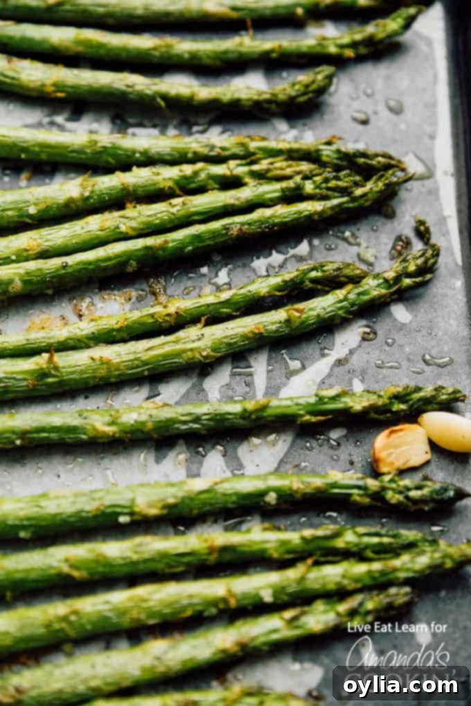 Close up photo of perfectly roasted asparagus spears on a sheet pan, seasoned with salt and pepper