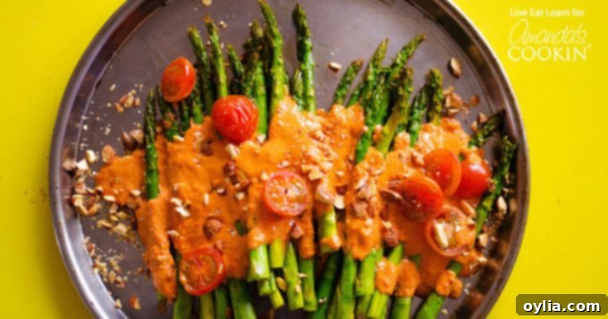 Delicious Roasted Asparagus side dish adorned with vibrant Smoky Romesco Sauce, fresh cherry tomatoes, and crunchy chopped almonds for a flavorful meal.