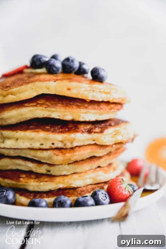 A vibrant stack of fluffy buttermilk pancakes generously topped with fresh blueberries and sliced strawberries.