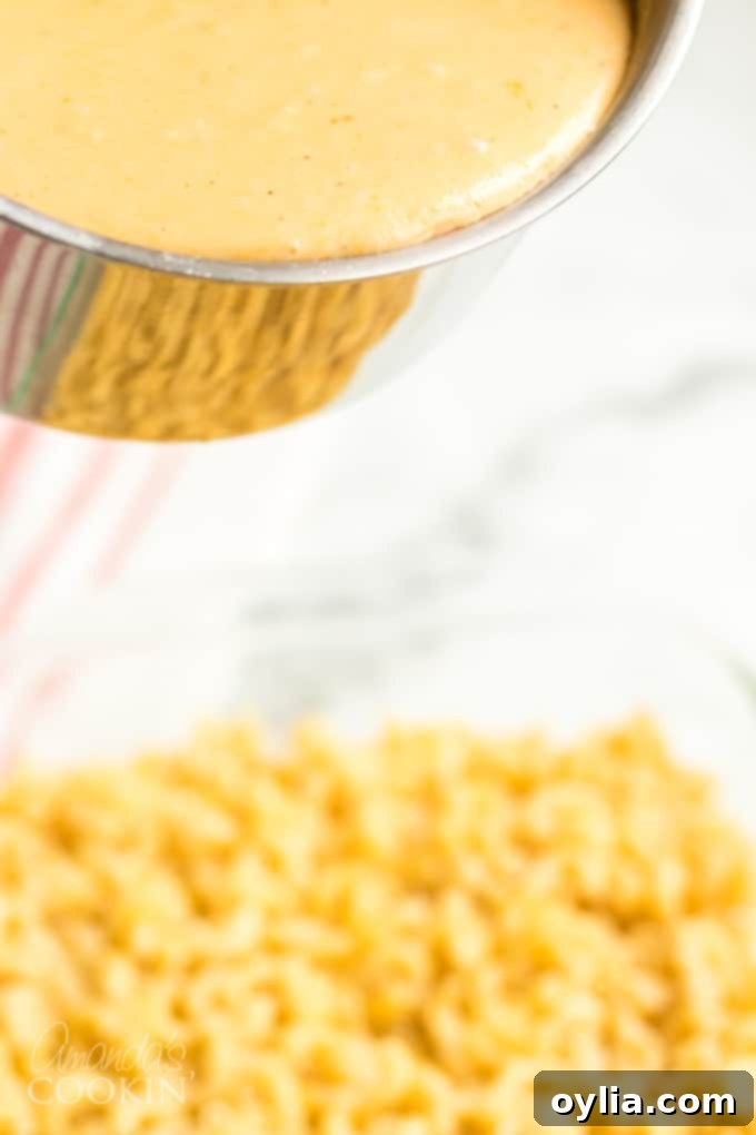Pouring rich cheese sauce over cooked elbow macaroni in a baking dish
