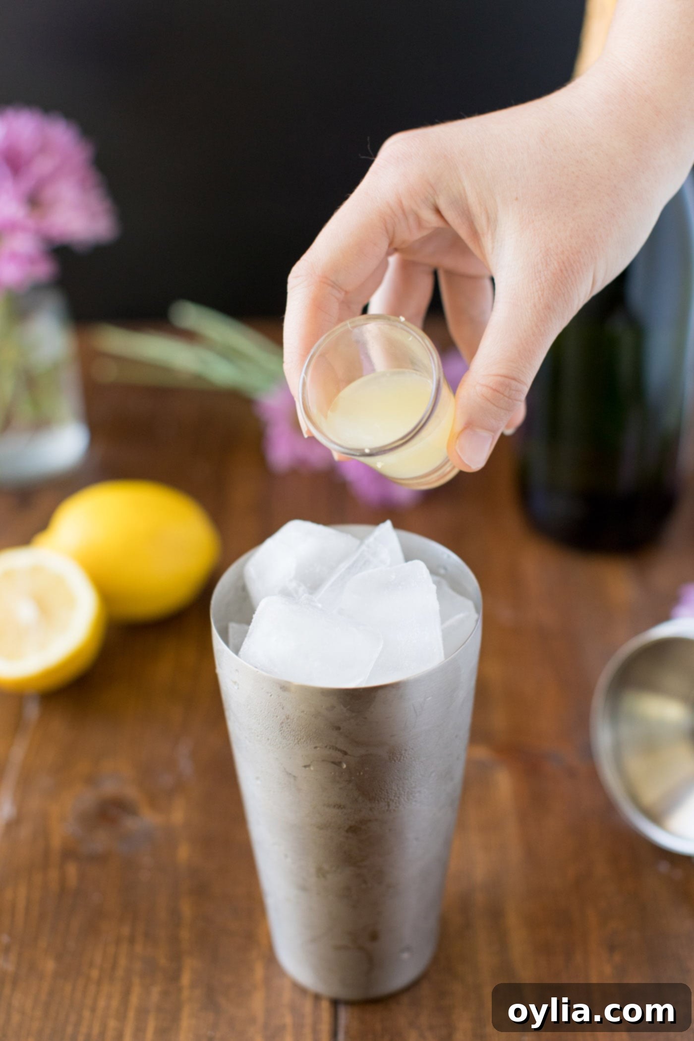 Pouring fresh lemon juice into a cocktail shaker with gin and simple syrup