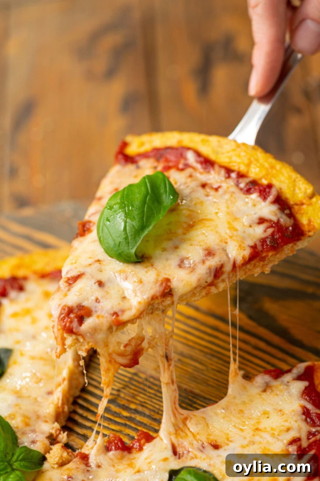 A delicious slice of homemade cauliflower pizza crust pizza being lifted from the platter, showing its firm structure and rich toppings.