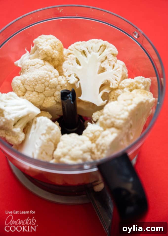 Cauliflower florets being processed in a food processor to achieve a fine, rice-like consistency, essential for a smooth pizza crust.