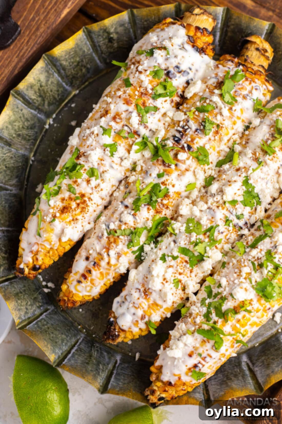 Mexican Corn on the Cob with Cheese, Mayo, and Latin Spices: The Best Summer Food! Enjoy this Mexican street food anytime with this easy recipe! #mexican #mexicancorn #cornonthecob #spices #latin #summer #summerfood #BBQ #grill Plate of Mexican street corn on the cob, garnished with cotija cheese, chili powder, and lime wedges.