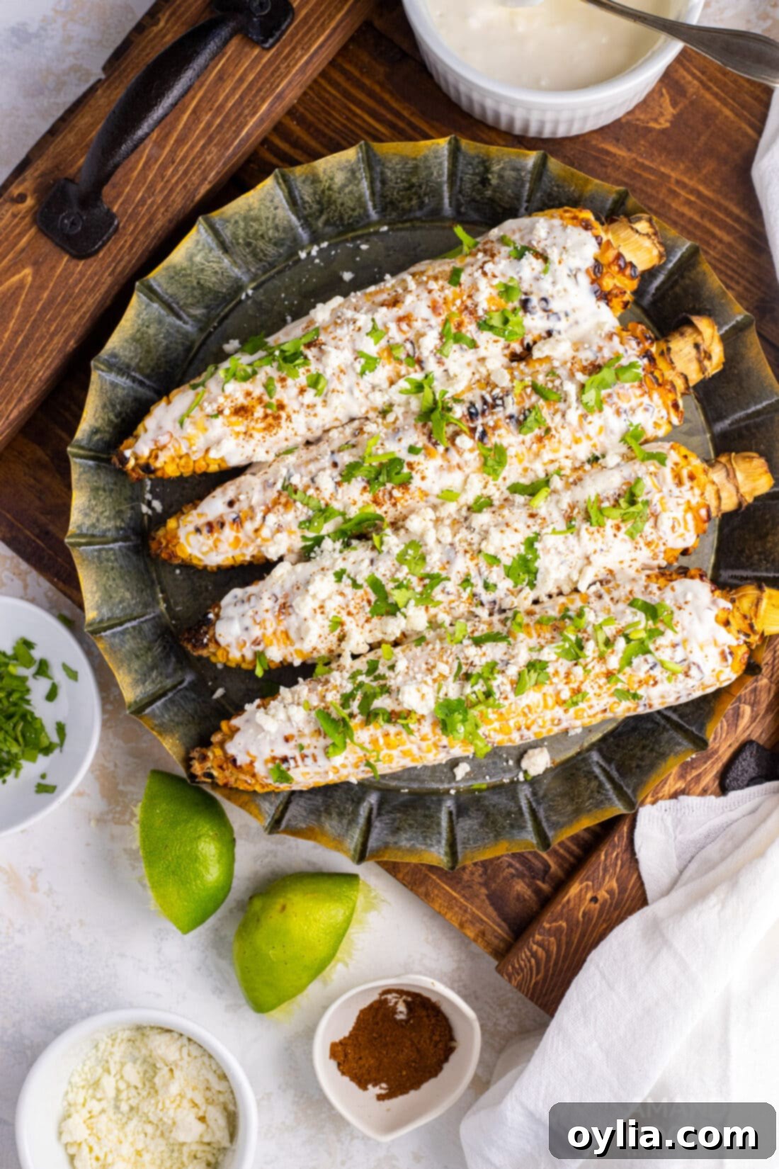 Mexican Corn on the Cob with Cheese, Mayo, and Latin Spices: The Best Summer Food! Enjoy this Mexican street food anytime with this easy recipe! #mexican #mexicancorn #cornonthecob #spices #latin #summer #summerfood #BBQ #grill Two pieces of Mexican street corn on a white plate, coated with mayo, cotija cheese, and chili powder.