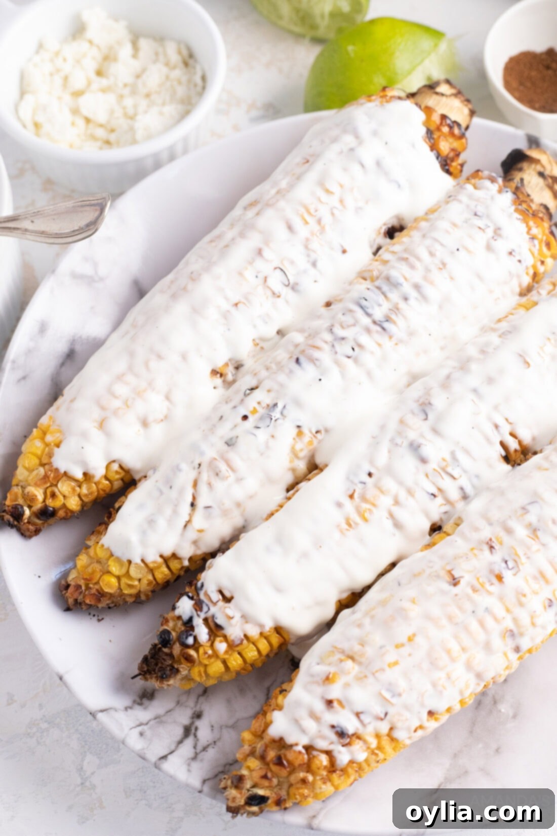 Mexican Corn on the Cob with Cheese, Mayo, and Latin Spices: The Best Summer Food! Enjoy this Mexican street food anytime with this easy recipe! #mexican #mexicancorn #cornonthecob #spices #latin #summer #summerfood #BBQ #grill Corn on the cob being brushed with mayonnaise, preparing it for the next layers of flavor.