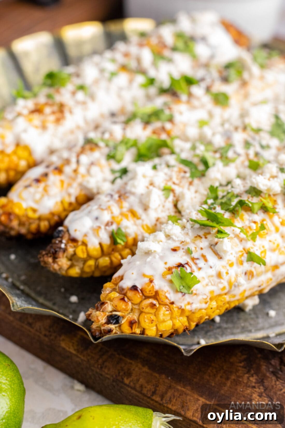 Mexican Corn on the Cob with Cheese, Mayo, and Latin Spices: The Best Summer Food! Enjoy this Mexican street food anytime with this easy recipe! #mexican #mexicancorn #cornonthecob #spices #latin #summer #summerfood #BBQ #grill Three pieces of Mexican street corn on the cob on a serving tray, garnished and ready to eat.