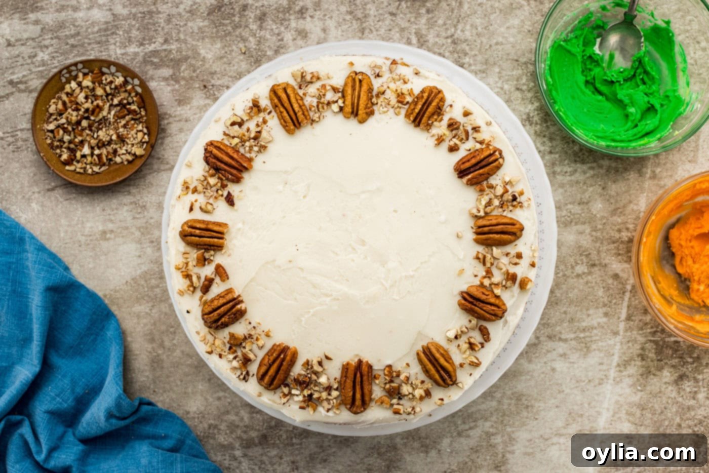 Twelve pecan halves and a scattering of chopped pecans neatly arranged on top of a frosted carrot cake.