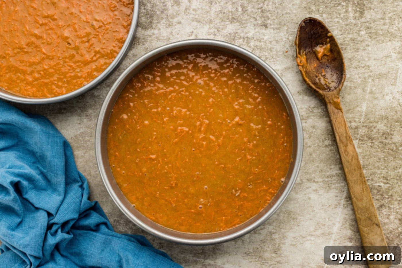 Smooth carrot cake batter evenly distributed in a round baking pan, ready for the oven.