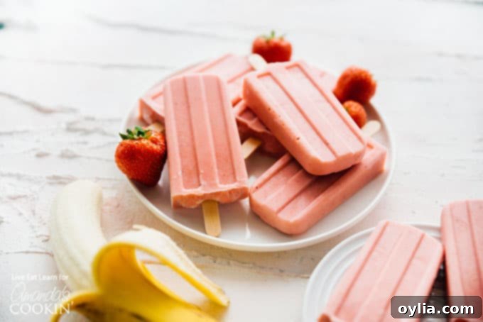 Two strawberry banana popsicles on a small white plate, showing their creamy texture.