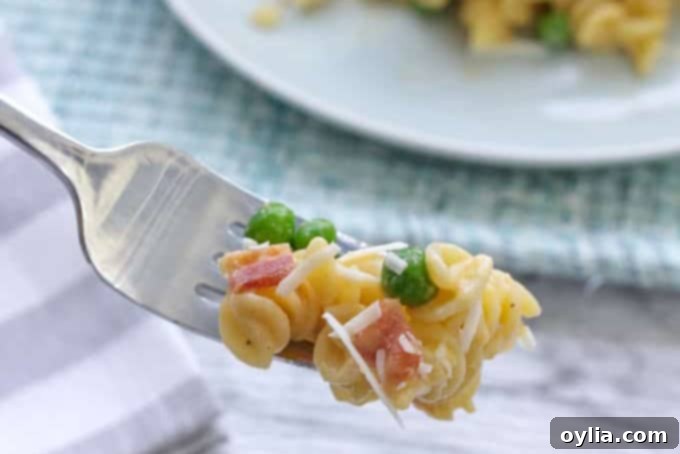 A fork with rotini pasta, peas, and bacon coated in a rich cheese sauce