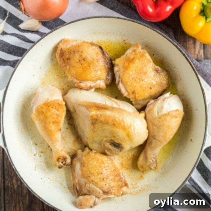 Chicken pieces expertly browned to a golden crisp in a large pan with olive oil.