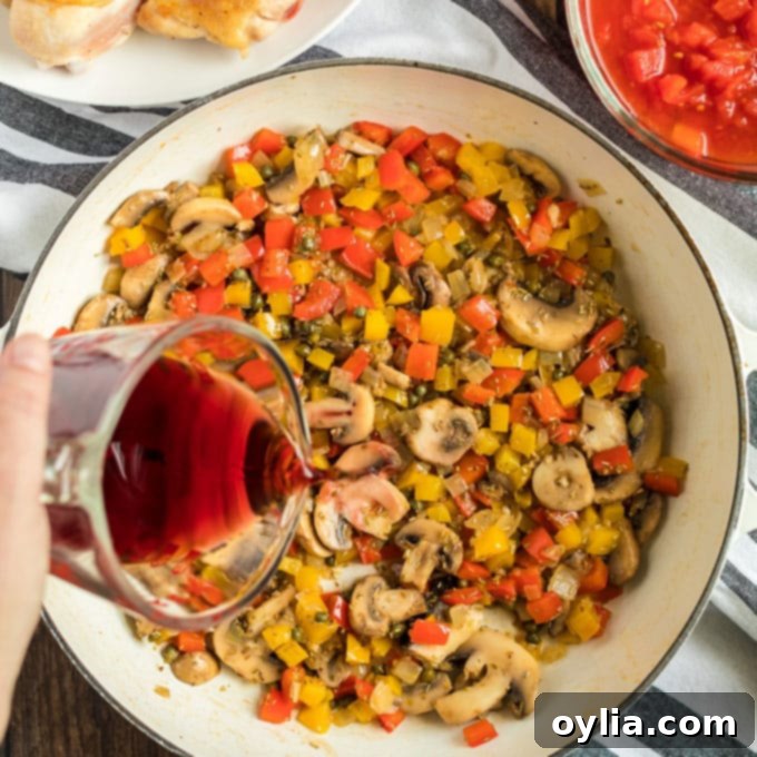 Red wine being poured into a skillet with sautéed vegetables, ready for deglazing.
