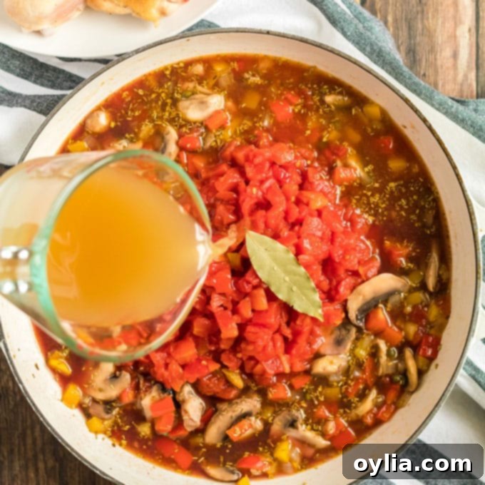 Diced tomatoes, chicken broth, and a bay leaf added to the simmering vegetables and wine in a skillet.