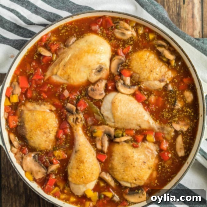 Browned chicken pieces nestled into a rich tomato and vegetable sauce in a pan, ready for simmering.