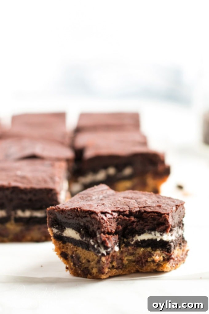 A slice of Slutty Brownie with a corner bitten off, showing the distinct layers of cookie, Oreo, and brownie.