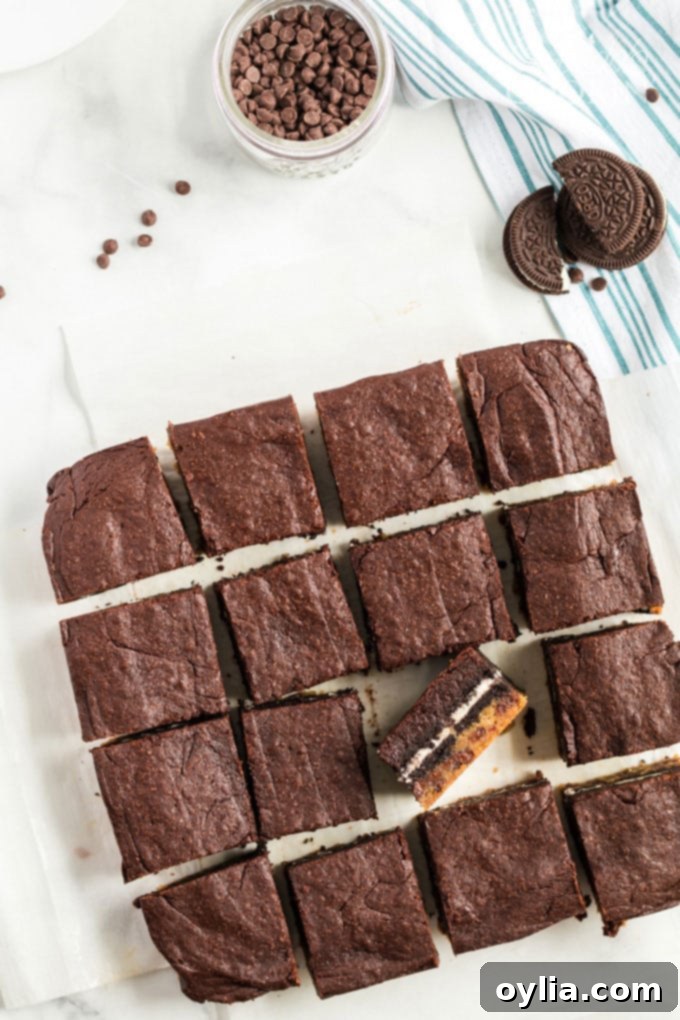 Overhead view of several perfectly sliced Slutty Brownies arranged on a cutting board, with one piece turned on its side to reveal the distinct cookie dough, Oreo, and brownie layers.