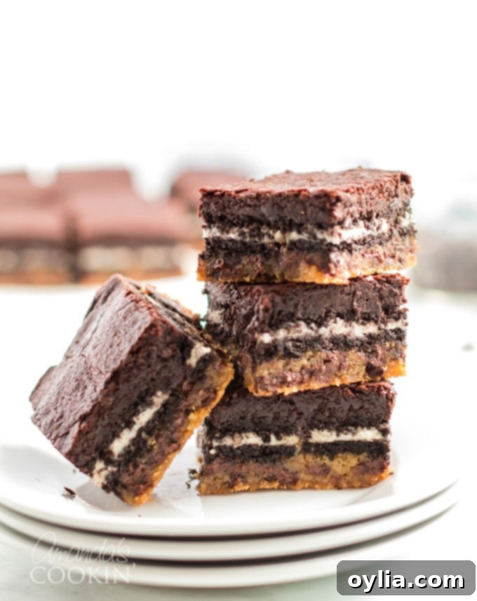 Stack of four Slutty Brownies, showing the distinct layers of chocolate chip cookie dough, Oreos, and fudgy brownies, presented on a dark surface.
