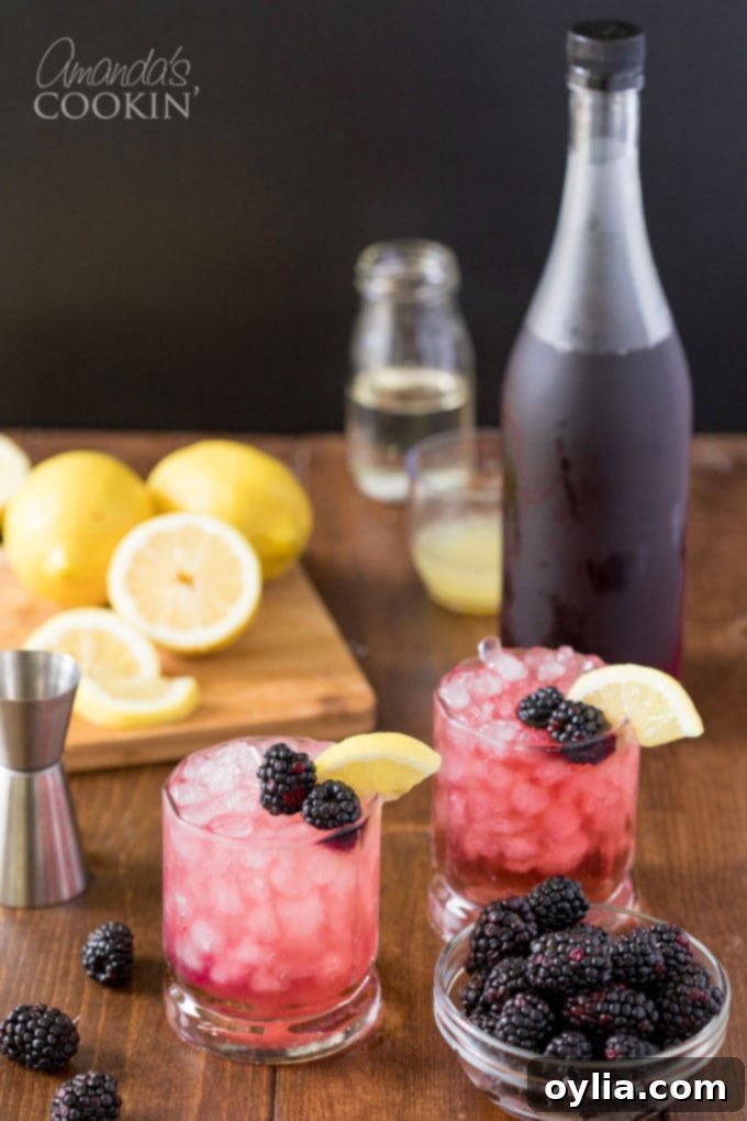 Two perfectly prepared Bramble cocktails presented with a bottle of blackberry liqueur in the background, emphasizing the key ingredient.