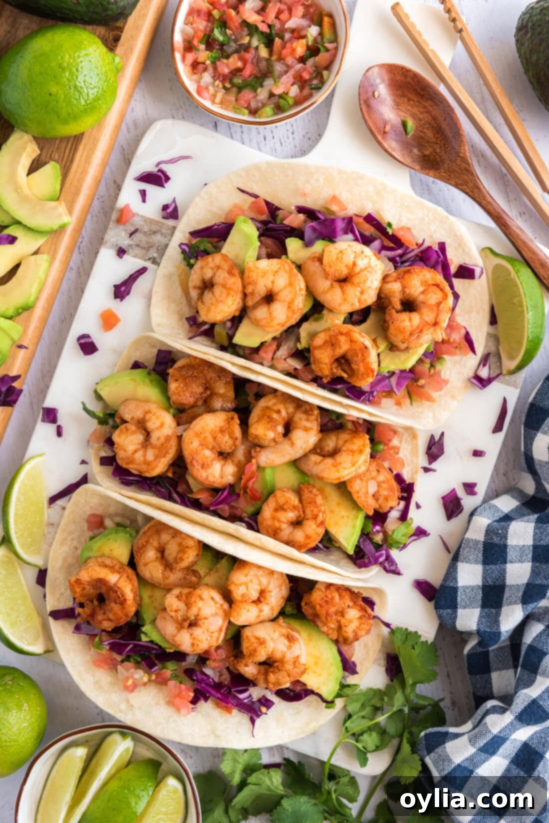Three perfectly assembled shrimp tacos, garnished with fresh limes and pico de gallo, inviting a delicious meal