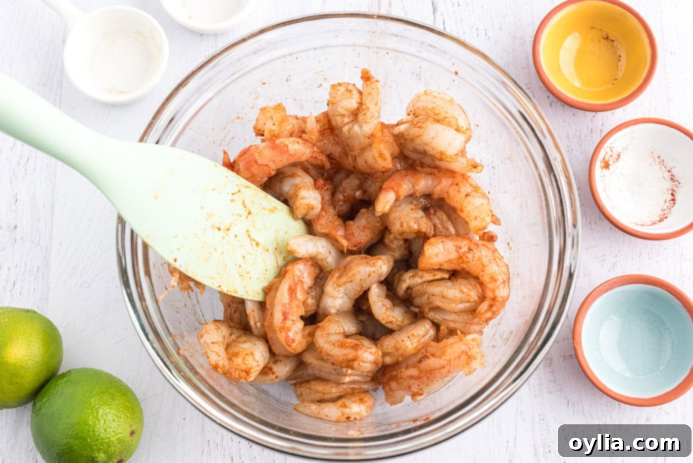 Seasoned raw shrimp in a bowl, ready for cooking, with a rubber spatula