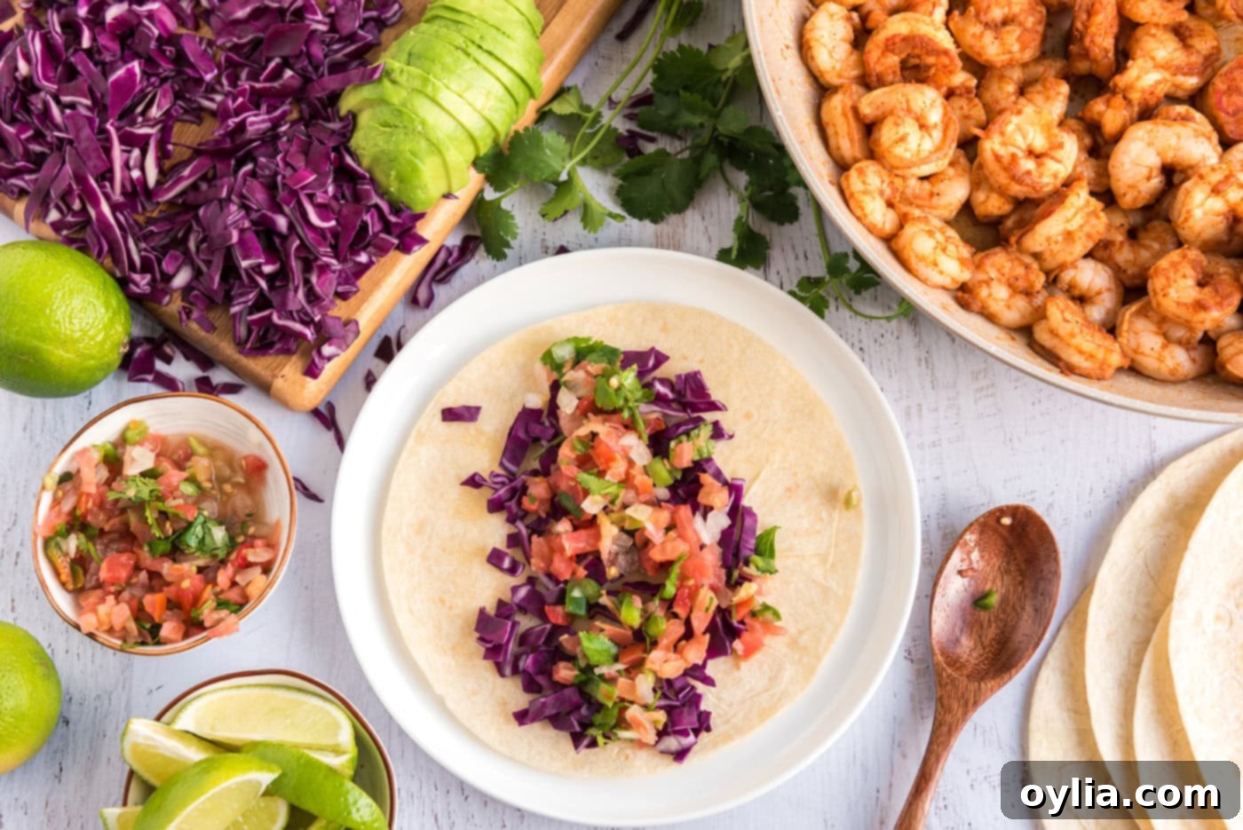 A corn tortilla being filled with cabbage, avocado, and fresh salsa, preparing for the shrimp