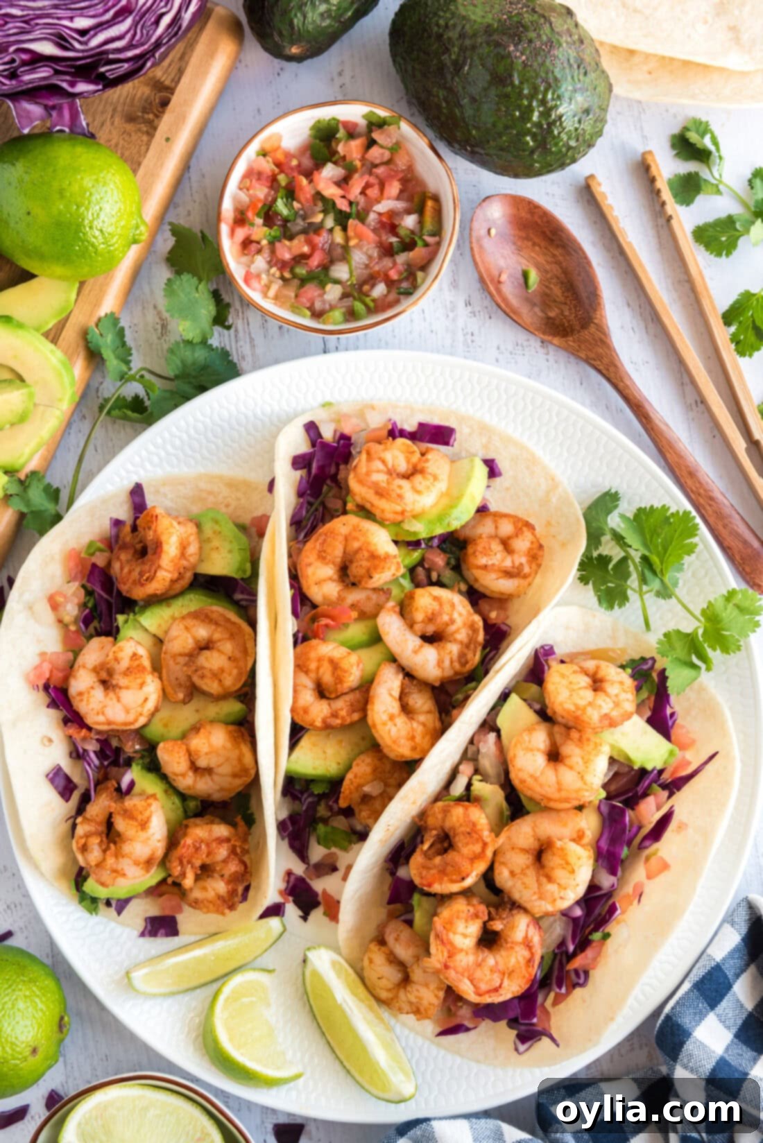 Three beautifully presented shrimp tacos on a pristine white plate, showcasing their fresh ingredients