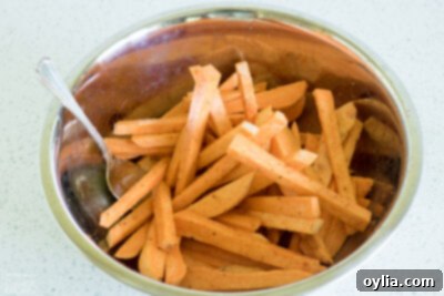 Sweet potato fries tossed with seasoning in a mixing bowl.