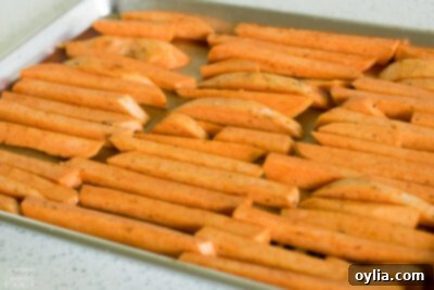 Sweet potato fries spread in a single layer on a baking sheet.
