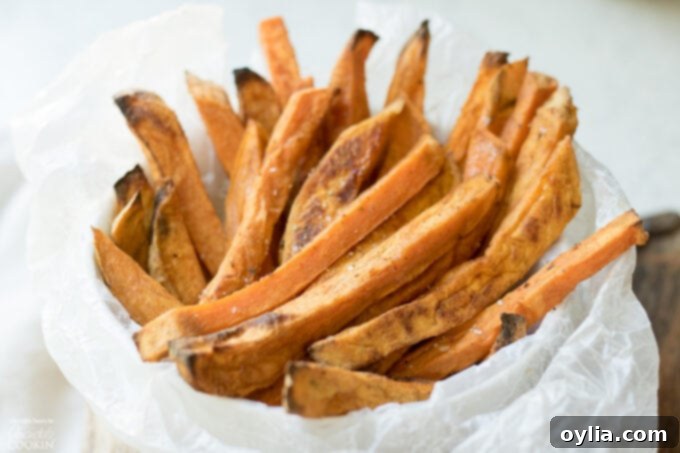 A large pile of freshly baked sweet potato fries in a white bowl.