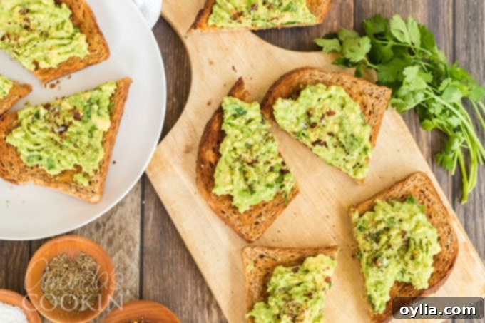 Overhead shot of two avocado toast slices on a wooden cutting board, ready to be served.