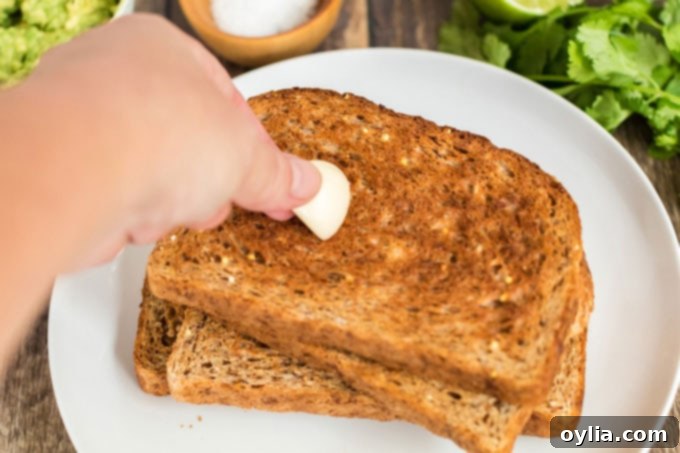 A hand rubbing a cut garlic clove over a slice of freshly toasted bread.