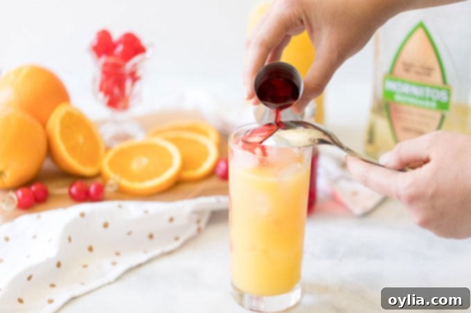 pouring grenadine syrup over the back of a spoon into a Tequila Sunrise glass