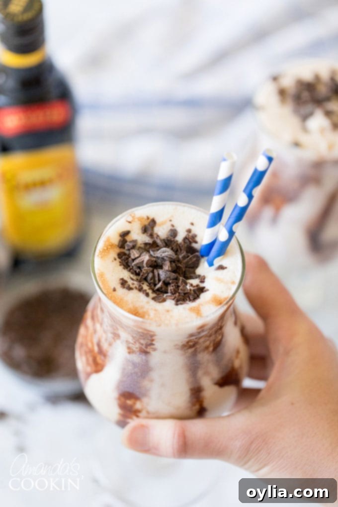 Hand holding a chilled hurricane glass filled with a creamy Frozen Mudslide cocktail.