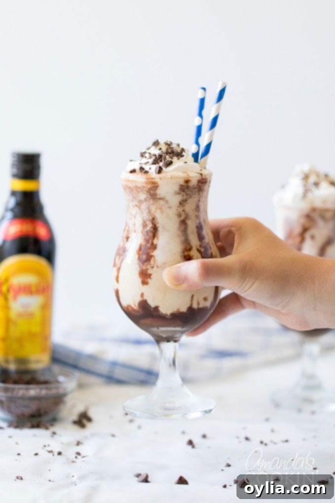 Hand holding a tall glass of a luscious Frozen Mudslide cocktail, ready to be enjoyed.